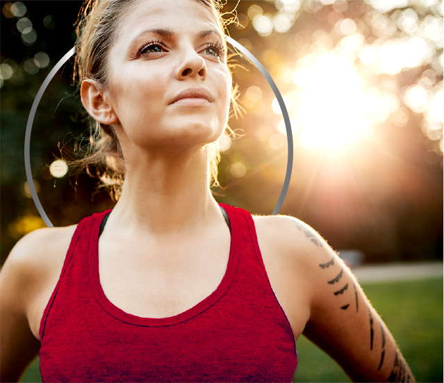 Active young woman wearing tank top and standing in empowered pose against a sunny backdrop