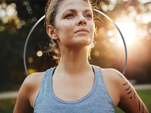 Active young woman wearing tank top, standing in empowered pose against a sunny backdrop